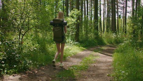 A-young-female-tourist-walks-through-the-forest-with-a-backpack-and-looks-at-the-beauty-of-nature.-Tourism-and-Hiking-adventures.-Beautiful-slender-woman-in-shorts-walking-through-the-woods
